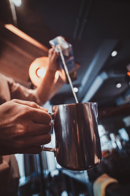 Il barista di talento sta versando il latte nella caraffa per il latte o il cappuccino al suo bar.