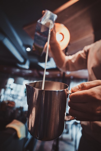 Il barista di talento sta versando il latte nella caraffa per il latte o il cappuccino al suo bar.