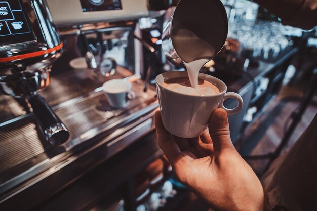 Il barista diligente sta preparando il latte fresco per i clienti per la pausa caffè in caffetteria.