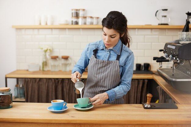 il barista femminile versa il latte, prepara due cappuccino, sembra concentrato.