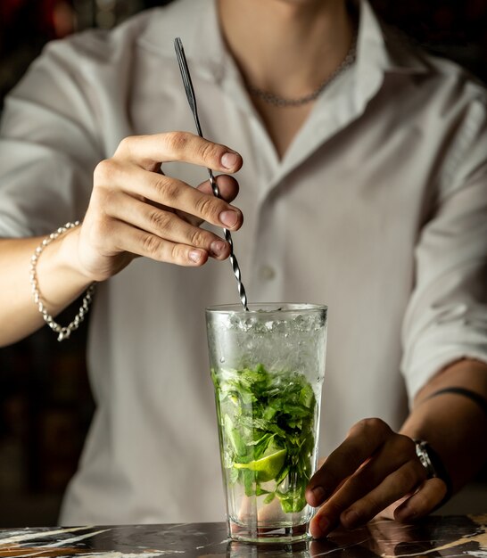 Il barista mescola il cocktail mojito con un cucchiaio di metallo