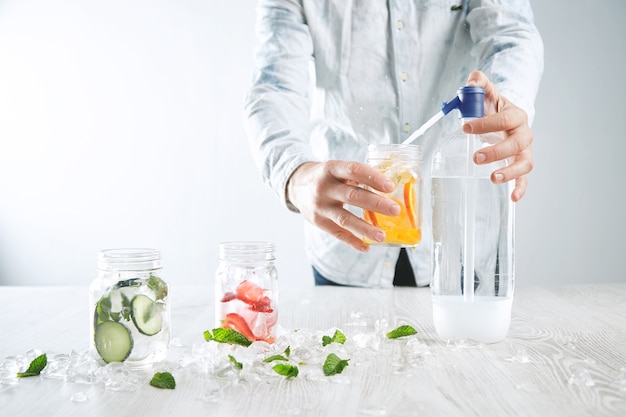 Il barista prepara la limonata fatta in casa, versa acqua frizzante in un barattolo rustico con fette d'arancia