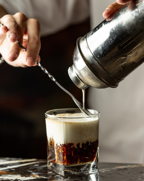 Il barista versa la crema nel caffè freddo con l'aiuto del cucchiaio