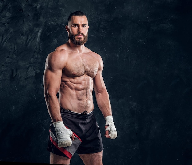 Il bel combattente muscoloso con il torso nudo sta dimostrando il suo potere in uno studio fotografico scuro.