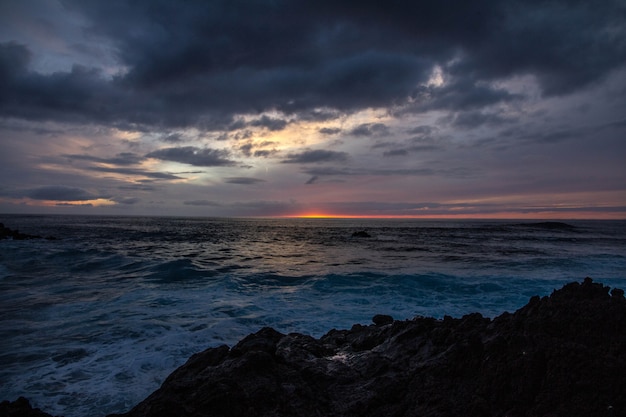 Il bello colpo del mare ondeggia vicino alle rocce sotto un cielo nuvoloso al tramonto