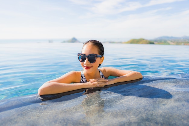 Il bello giovane sorriso asiatico della donna del ritratto felice si rilassa intorno alla piscina nella località di soggiorno dell&#39;hotel per svago