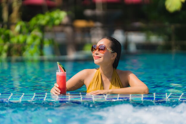 Il bello giovane svago asiatico della donna del ritratto si rilassa sorriso con il succo dell&#39;anguria intorno alla piscina nella località di soggiorno dell&#39;hotel