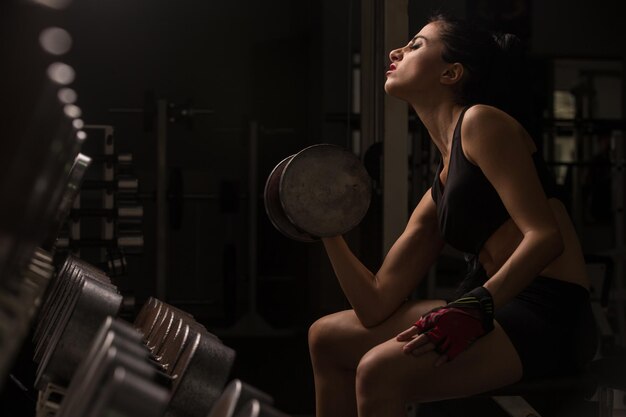 Il bodybuilder di giovane bella bionda sexy dell'atleta si esercita in palestra in bello abbigliamento sportivo su uno sfondo scuro