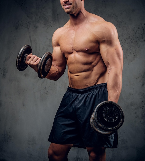 Il bodybuilder sorridente felice sta facendo esercizi con i barbi e mostra i suoi muscoli sullo sfondo scuro.