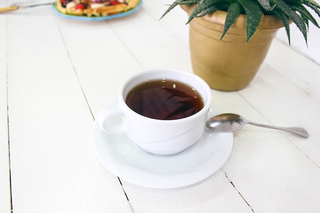 Il caffe di seduta della ragazza che mangia la cialda della prima colazione con la salsa di cioccolato, le fette della banana e le fragole sul piatto ceramico verde e ha fotografato la sua prima colazione