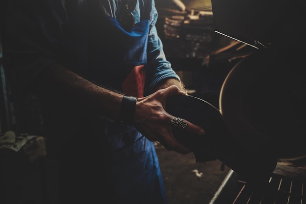 Il calzolaio in grembiule sta lavorando sulla scarpa utilizzando una macchina speciale nella sua officina.