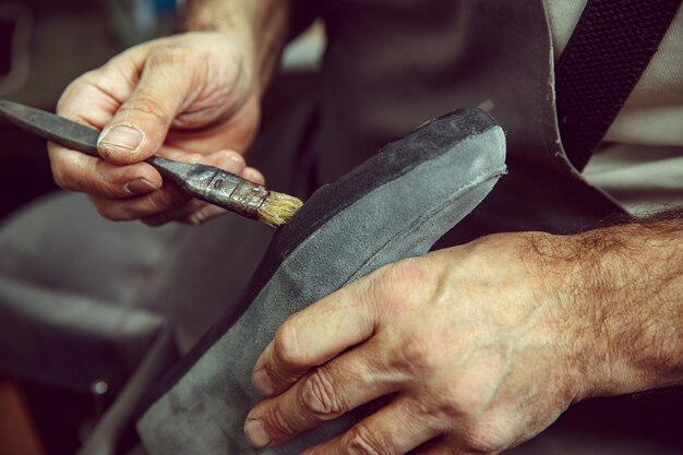 Il calzolaio produce scarpe da uomo. Spalma il liquido speciale con un pennello. L'uomo nella professione femminile. Concetto di uguaglianza di genere