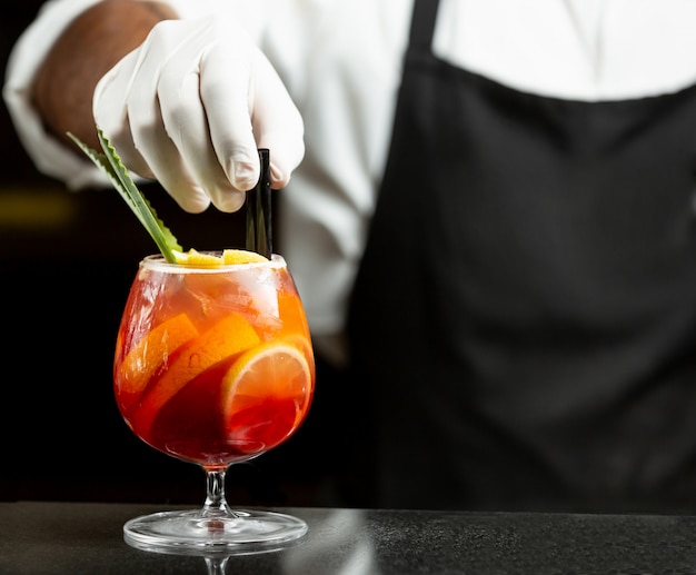 Il cameriere mette le cannucce di plastica nel cocktail di sangria in vetro