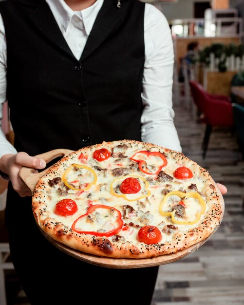 Il cameriere tiene la pizza di carne con peperoni rossi gialli pomodoro e formaggio