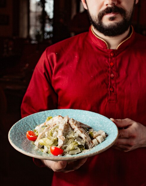 Il cameriere tiene un'insalata caesar con lattuga di pollo, pomodorini, parmigiano e ripieno di pane