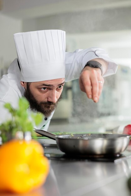 Il capo chef guarnisce una deliziosa cena gourmet con parmigiano nella cucina del ristorante. Lavoratore dell'industria alimentare caucasica che cucina con erbe fresche e verdure biologiche.