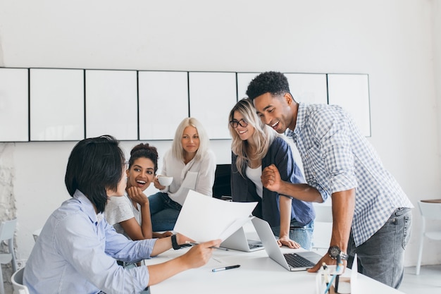 Il capo dipartimento africano è soddisfatto del lavoro del personale. Studente maschio asiatico in camicia alla moda che dice agli amici dell'università circa il suo rapporto di scienza.