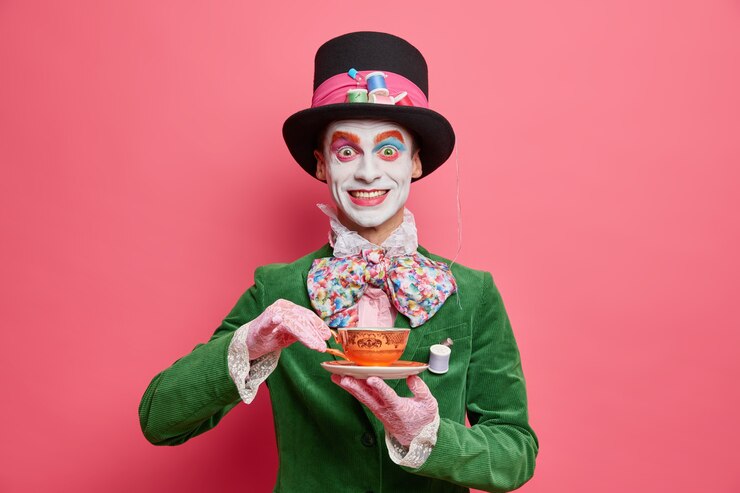 Foto gratuito il cappellaio maschio positivo gode di un tea party vestito con cappello e giacca di velluto verde in posa contro il muro roseo sembra un vero gentiluomo