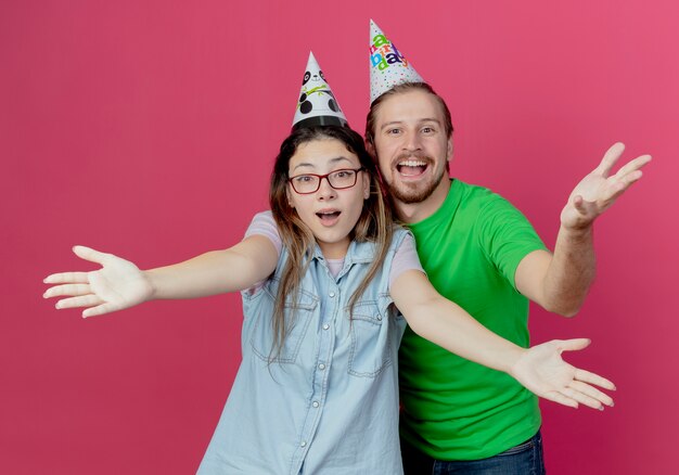 Il cappello da portare delle giovani coppie allegre sembra alzare le mani isolate sulla parete rosa