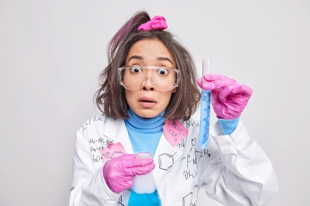 Il chimico femminile utilizza l'attrezzatura di laboratorio per l'esperimento mescola i reagenti ottiene soluzioni blu discon qualcosa vestito in uniforme isolato su bianco