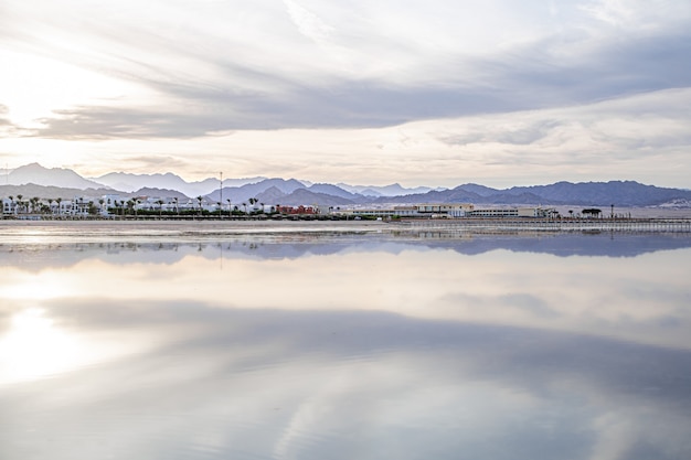 Il cielo del paesaggio si riflette nel mare. Costa della città con le montagne all'orizzonte.