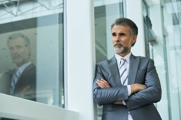 Il colpo medio dell'uomo d'affari che sta con le armi ha piegato appoggiarsi la struttura della finestra