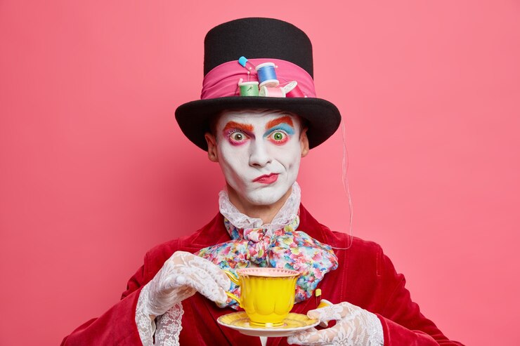 Foto gratuito il colpo orizzontale del cappellaio maschio serio pone con la tazza di tè indossa il cappello ha modi di abiti da gentiluomo aristocratici per le pose di carnevale mascherato al coperto