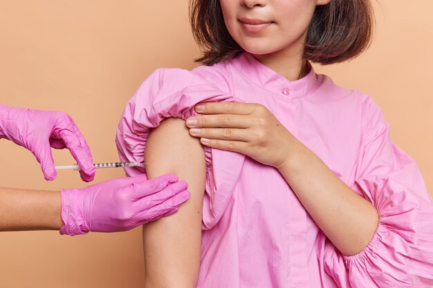 Il colpo ritagliato di una donna irriconoscibile fa la vaccinazione in clinica indossa una camicetta rosa e si prende cura della sua salute durante la pandemia