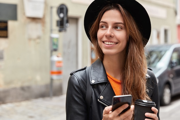 Il colpo schietto della donna caucasica felice ha un sorriso gentile sul viso, beve caffè dal bicchiere di carta