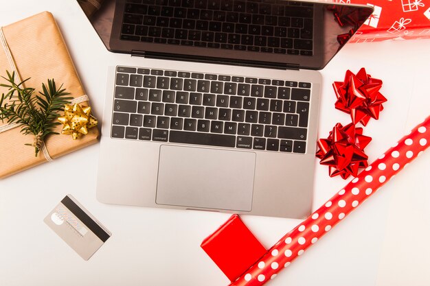 Il computer portatile e la carta di credito con Natale hanno avvolto il regalo sulla tavola