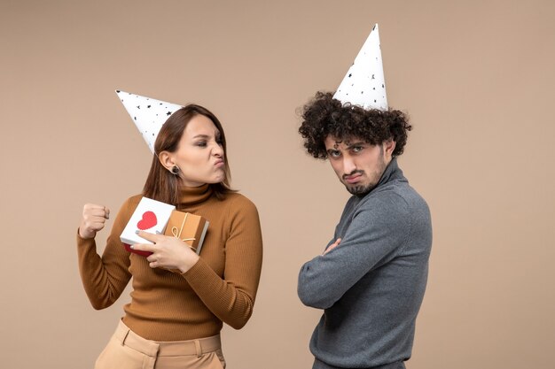 Il concetto del nuovo anno con la bella giovane coppia indossa la ragazza nervosa del cappello del nuovo anno con il cuore e il regalo