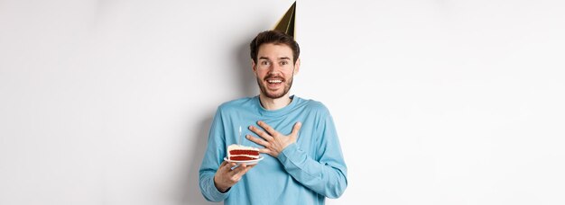 Il concetto di celebrazione e festività ha sorpreso il ragazzo di compleanno con il cappello da festa che tiene la torta di compleanno e guarda t