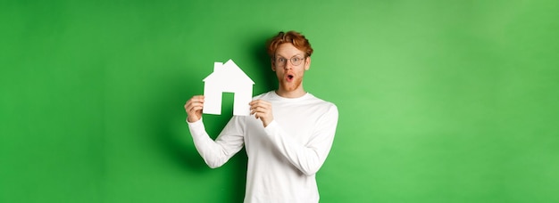 Il concetto di proprietà immobiliare e di acquisto ha sorpreso il giovane uomo dai capelli rossi che mostra il modello della casa di carta e lo