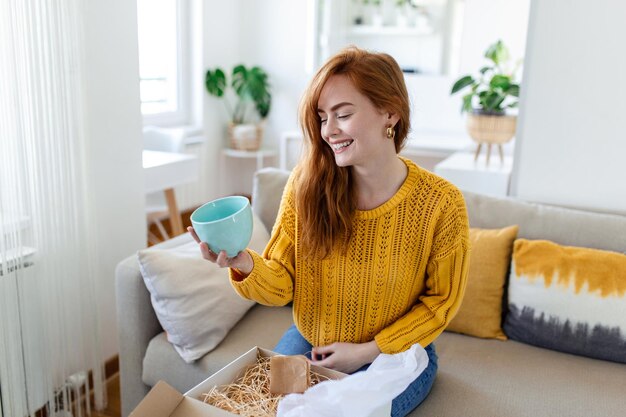 Il consumatore femminile disimballa il pacco riceve l'acquisto al dettaglio di spedizione postale veloce concetto di consegna Bella giovane donna tiene in mano una scatola di cartone seduta sul divano a casa