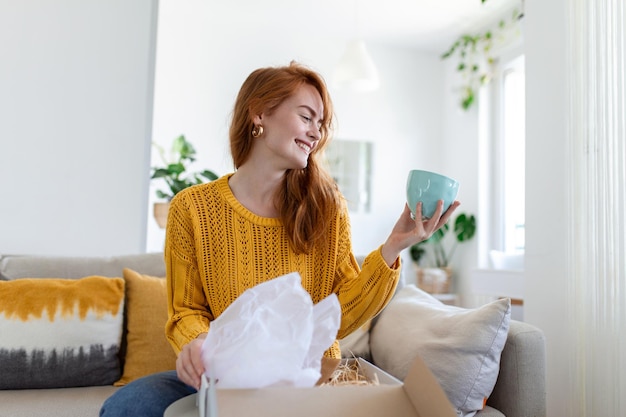 Il consumatore femminile disimballa il pacco riceve l'acquisto al dettaglio di spedizione postale veloce concetto di consegna Bella giovane donna tiene in mano una scatola di cartone seduta sul divano a casa