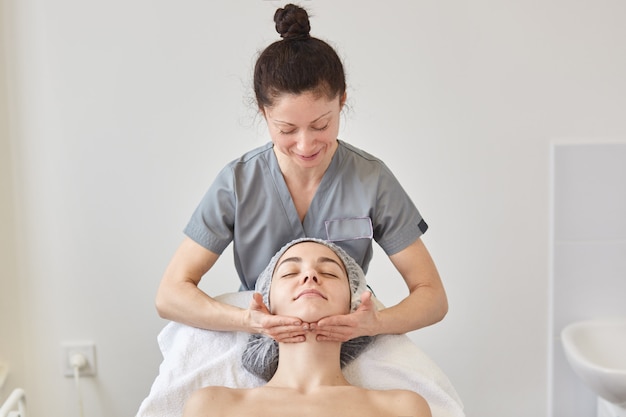 Il cosmetologo indossa un abito grigio che massaggia il viso del paziente.