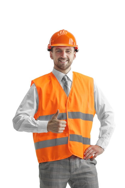 Il costruttore in un giubbotto di costruzione e casco arancione in piedi sul muro bianco. Specialista della sicurezza, ingegnere, industria, architettura, manager, occupazione, uomo d'affari, concetto di lavoro