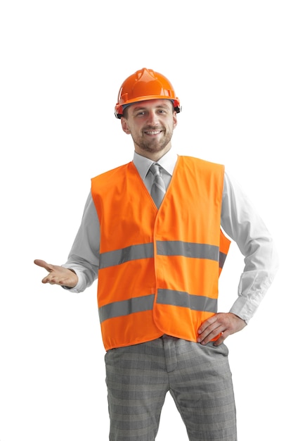 Il costruttore in un giubbotto di costruzione e casco arancione in piedi sul muro bianco. Specialista della sicurezza, ingegnere, industria, architettura, manager, occupazione, uomo d'affari, concetto di lavoro