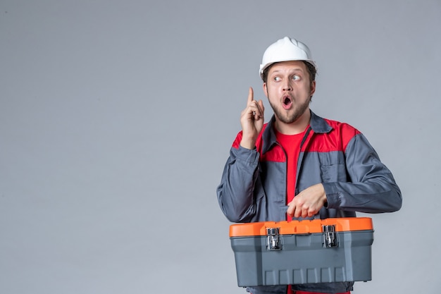 il costruttore maschio di vista frontale in valigetta degli attrezzi di tenuta uniforme ha un'idea su sfondo grigio