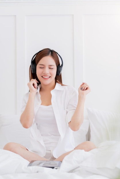 Il costume del vestito bianco della donna asiatica di felicità gode di musica d'ascolto di ballo con lo sfondo della camera da letto delle cuffie