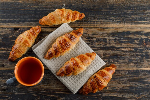 Il croissant con una tazza di tè piatto giaceva sul telo da cucina e in legno