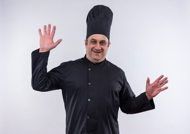 Il cuoco maschio di mezza età soddisfatto in uniforme del cuoco unico allarga le mani sulla parete bianca isolata