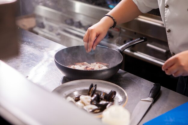 Il cuoco maschio frigge i frutti di mare ai fornelli nel ristorante della cucina