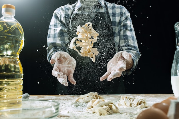 Il cuoco maschio professionista spruzza la pasta con farina, i preapares o cuoce il pane al tavolo da cucina