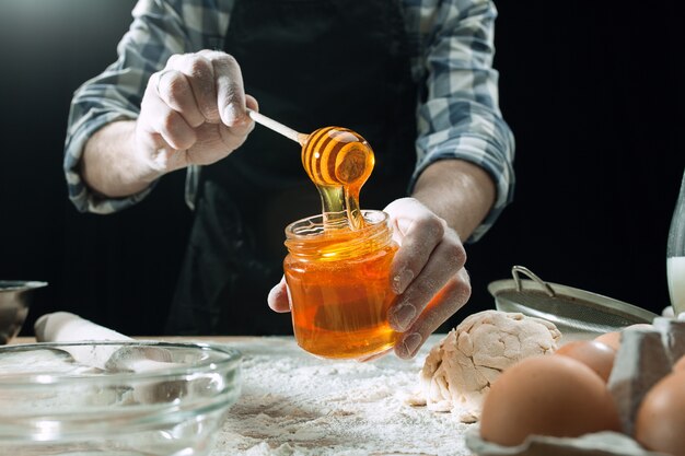 Il cuoco maschio professionista spruzza la pasta con farina, i preapares o cuoce il pane al tavolo da cucina