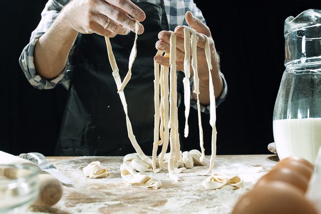 Il cuoco professionista maschio spruzza la pasta con farina, preapares o cuoce il pane al tavolo della cucina