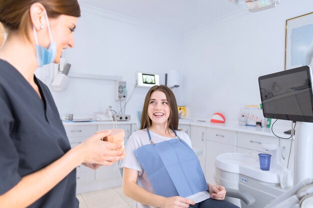 Il dentista femminile che mostra i denti modella al paziente sorridente