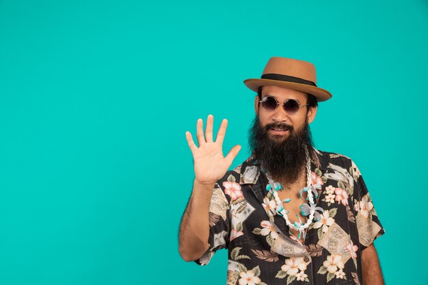 Il di un uomo felice con una lunga barba che indossa un cappello, indossa una camicia a righe che mostra un gesto su un blu.