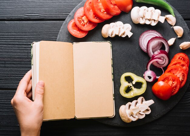 Il diario della tenuta della mano di una persona vicino affettato le verdure sul contesto di legno nero