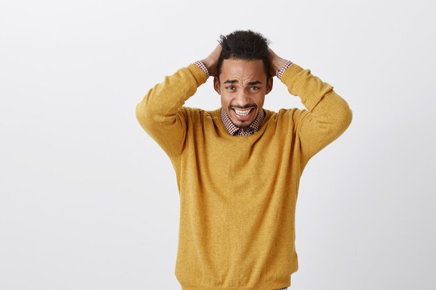 Il disastro è avvenuto con un povero studente. Giovane uomo dalla pelle scura frustrato scontento con taglio di capelli afro che si tiene per mano dietro la testa, soffre di dolore emotivo, accigliato per la disperazione e la tristezza